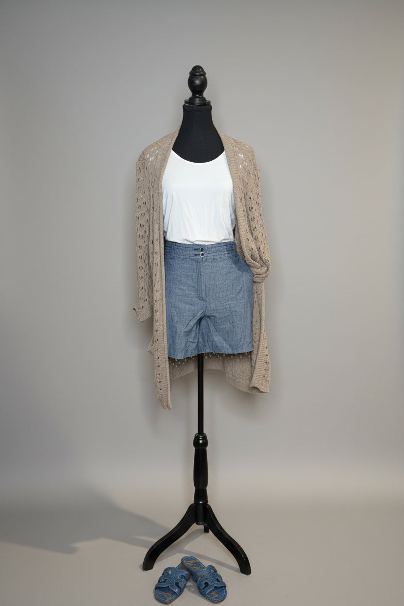 Mannequin wearing a beige cardigan, white shirt, and blue shorts against a gray wall.