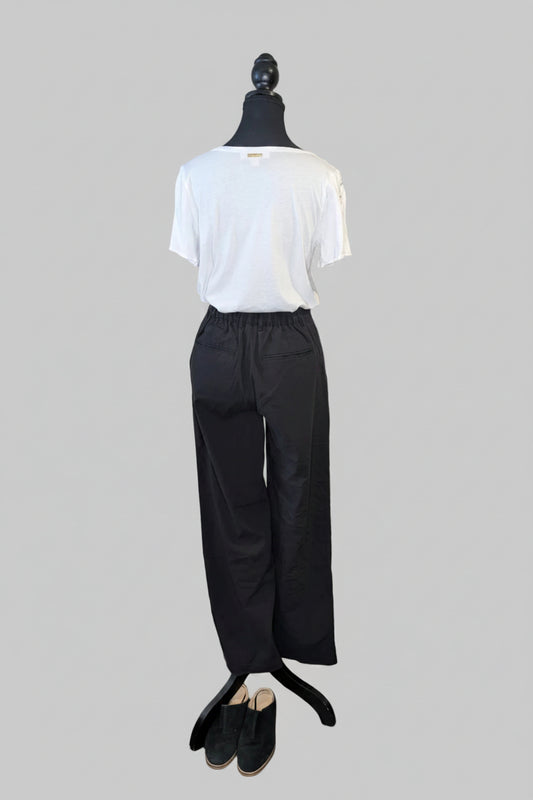 Mannequin wearing a white shirt and black pants against a plain wall.