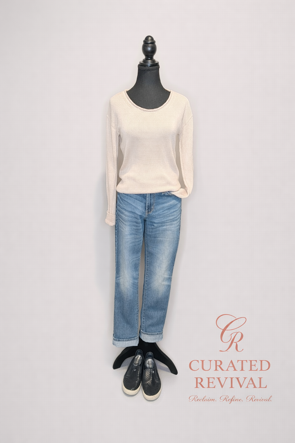 Mannequin wearing a cream sweater, blue jeans, and black shoes with 'Curated Revival' branding.