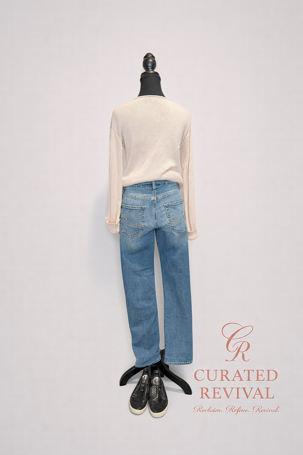 Mannequin wearing a cream sweater and blue jeans with 'Curated Revival' branding on a light gray background.