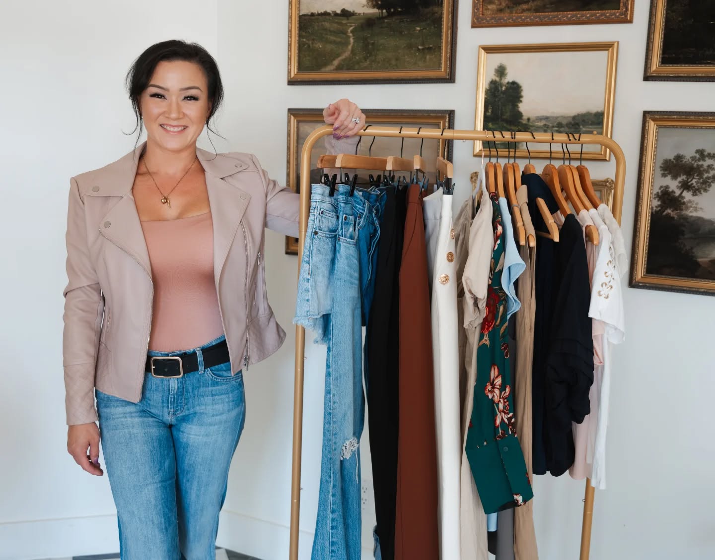 Woman standing next to a rack of clothes in a room with framed pictures on the wall.