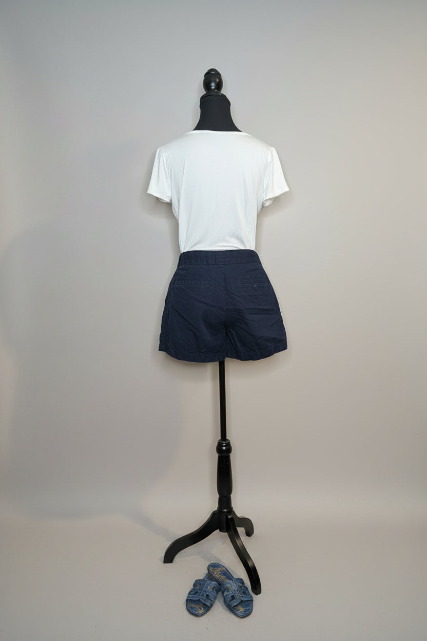 Mannequin wearing a white t-shirt and navy shorts against a gray wall with shoes on the floor.