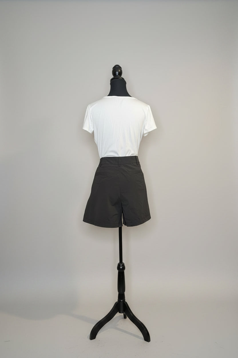 Mannequin wearing a white shirt and gray shorts against a gray wall.