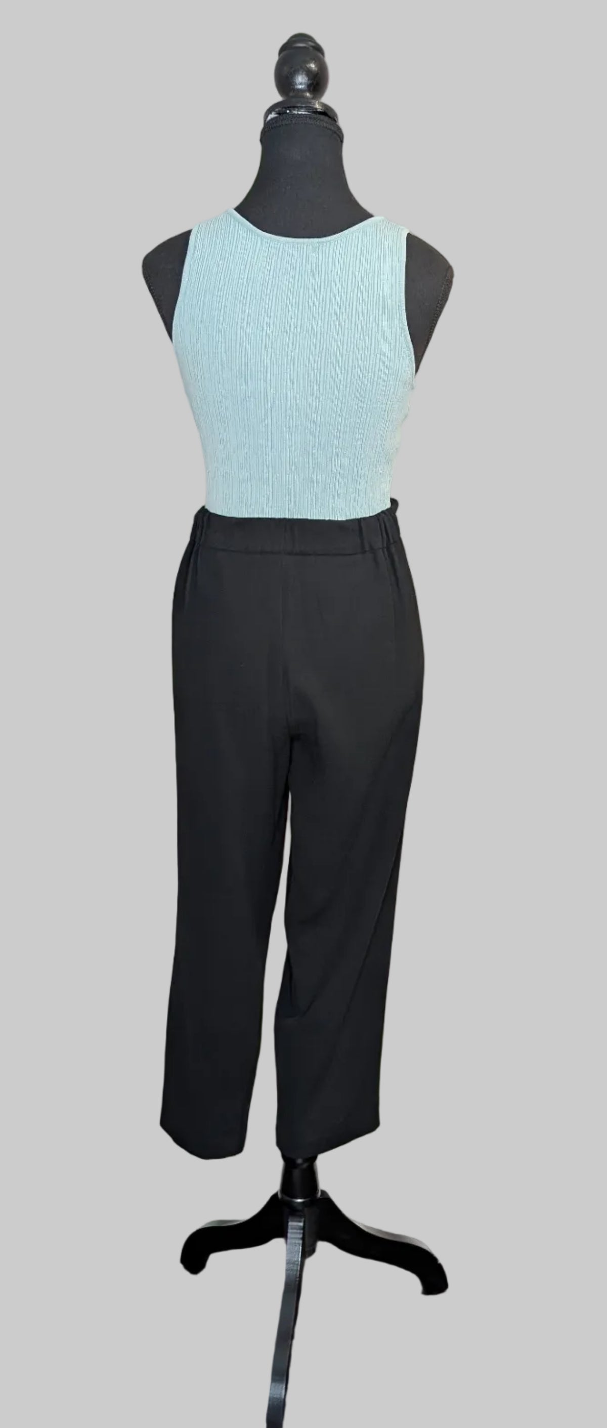 Mannequin wearing a light blue top and black pants against a plain wall.