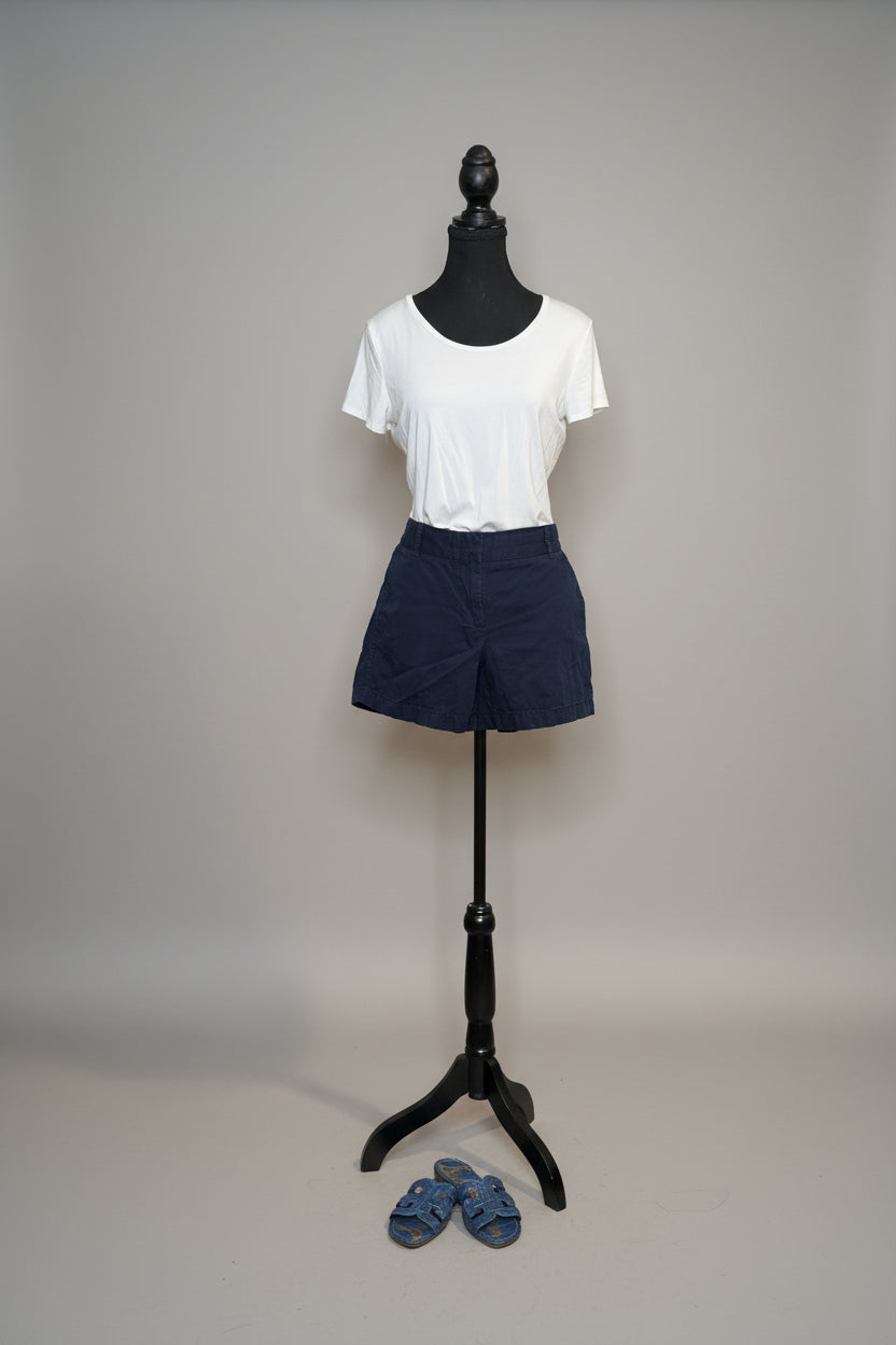 Mannequin wearing a white t-shirt and navy shorts with a vase of flowers and slippers in the background.