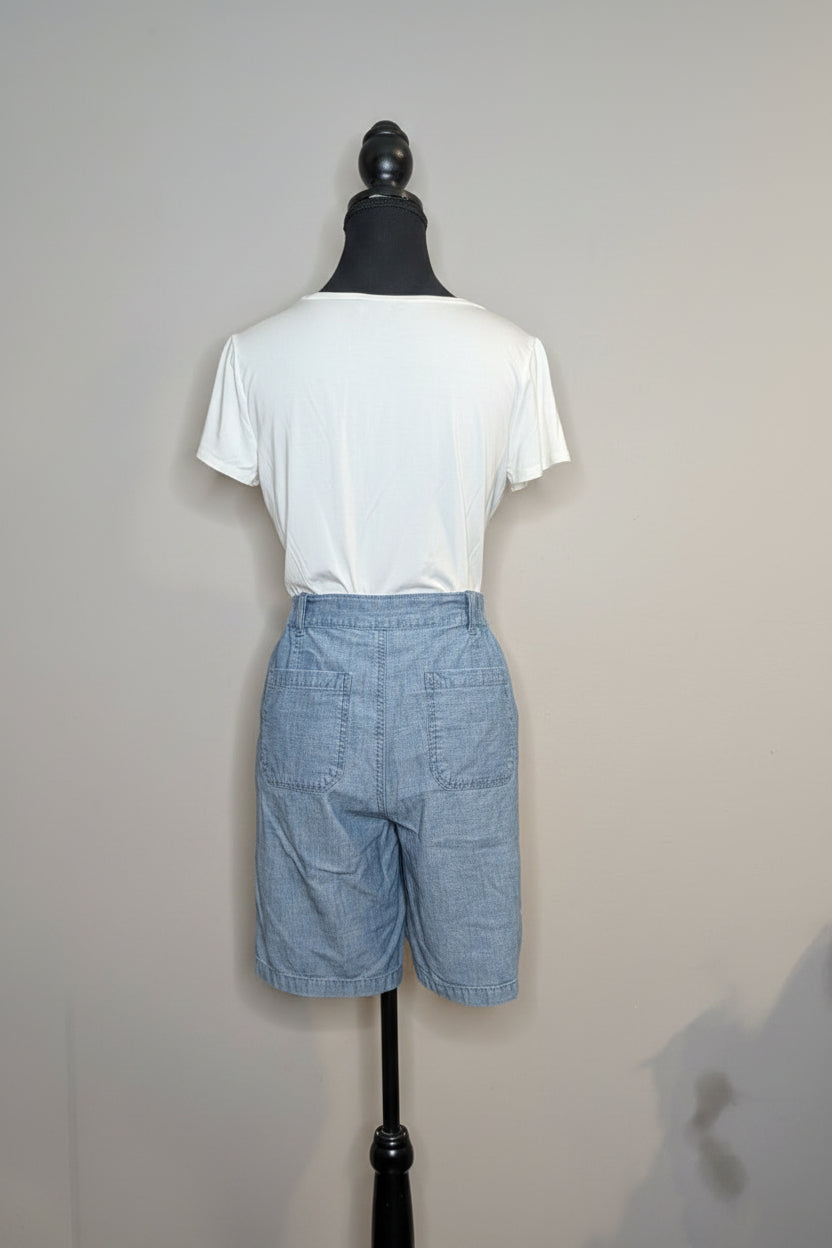 Mannequin wearing a white shirt and blue shorts in a room with a door and decorative items.
