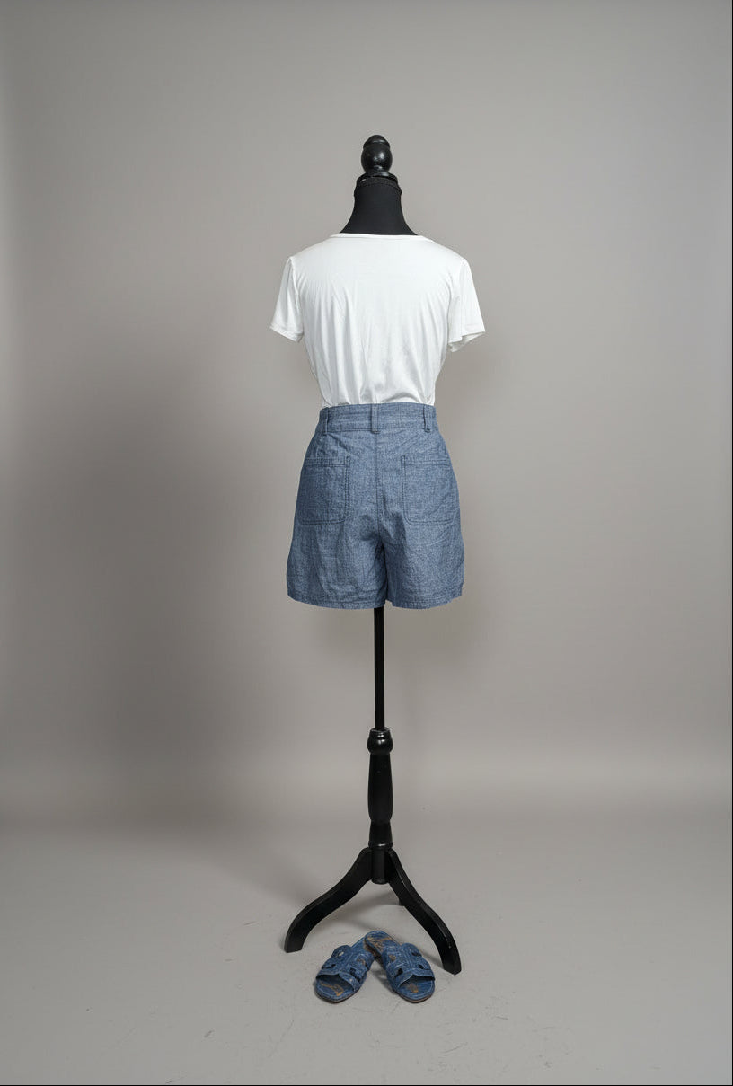 Mannequin wearing a white shirt and blue shorts against a neutral wall with decorative elements.
