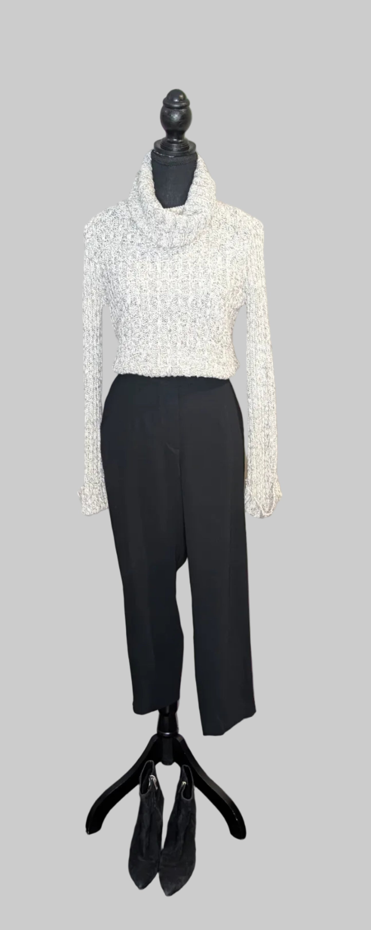 Mannequin wearing a white turtleneck sweater and black pants on a gray background