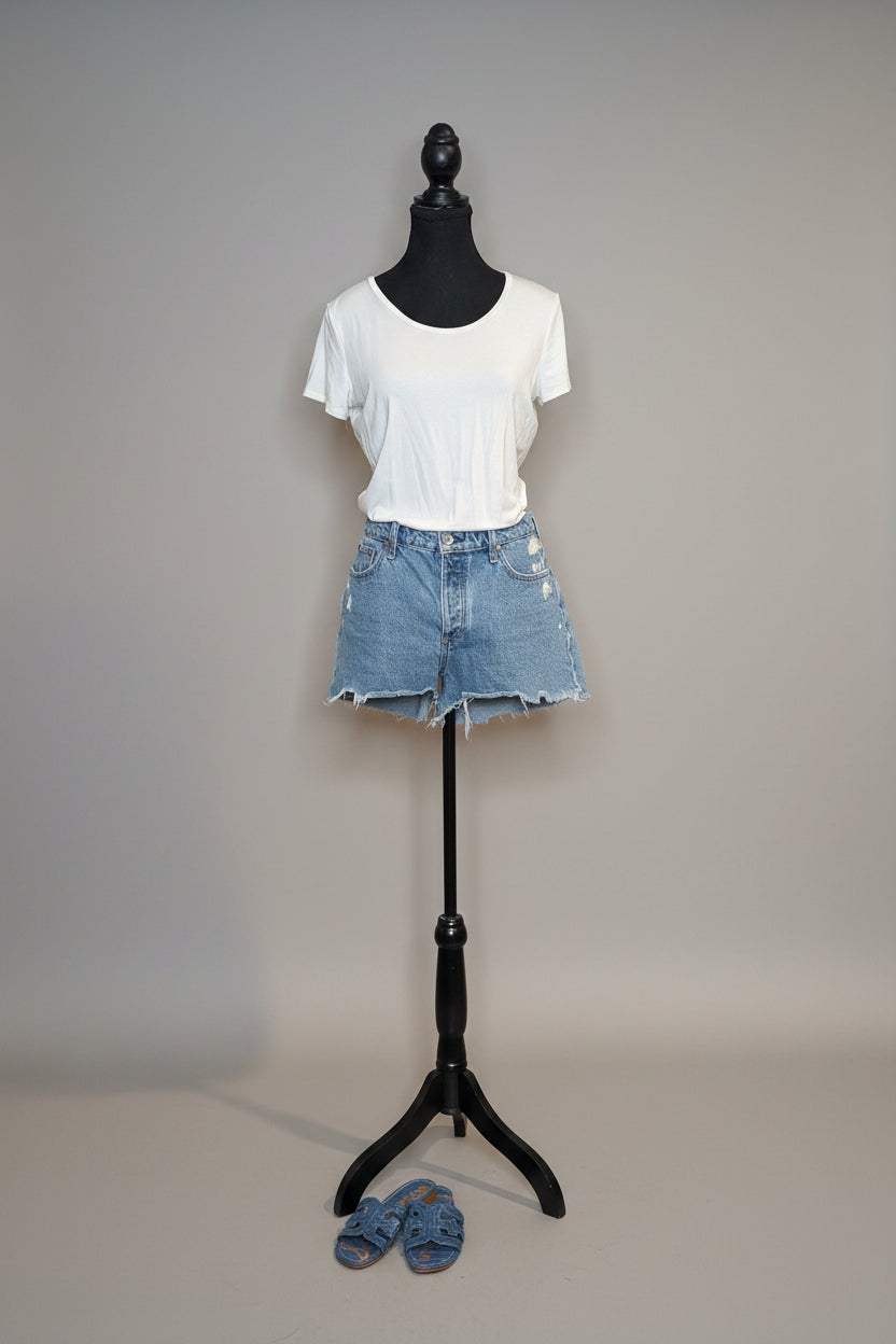 Mannequin wearing a white t-shirt and denim shorts against a plain wall.