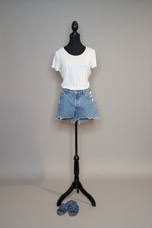 Mannequin wearing a white t-shirt and denim shorts against a plain wall.
